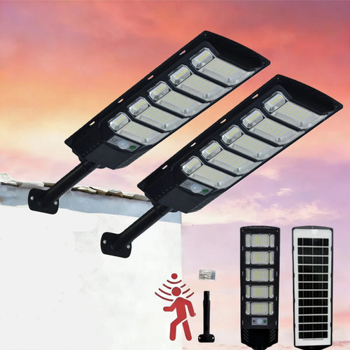 Two black solar LED street lights mounted on a wall against a sunset sky, showing front and solar panel backs.