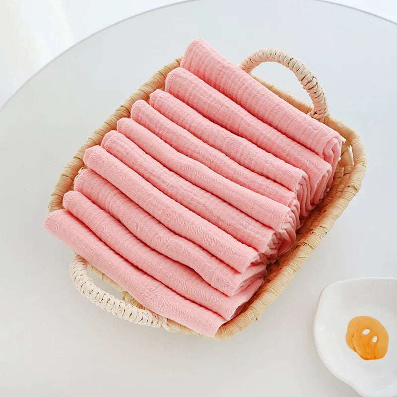 Set of soft pink baby care muslin cloths folded in a decorative wicker basket.