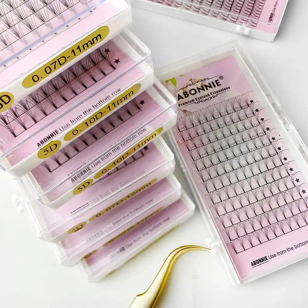 Stack of ABONNIE premade volume eyelash extension trays in pink packaging, with black fan lashes and a gold tweezer.