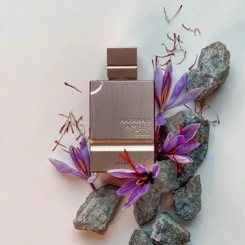 Haramain Amber Oud Rouge perfume bottle in a rectangular rose-gold metal case, surrounded by saffron and gray rocks.