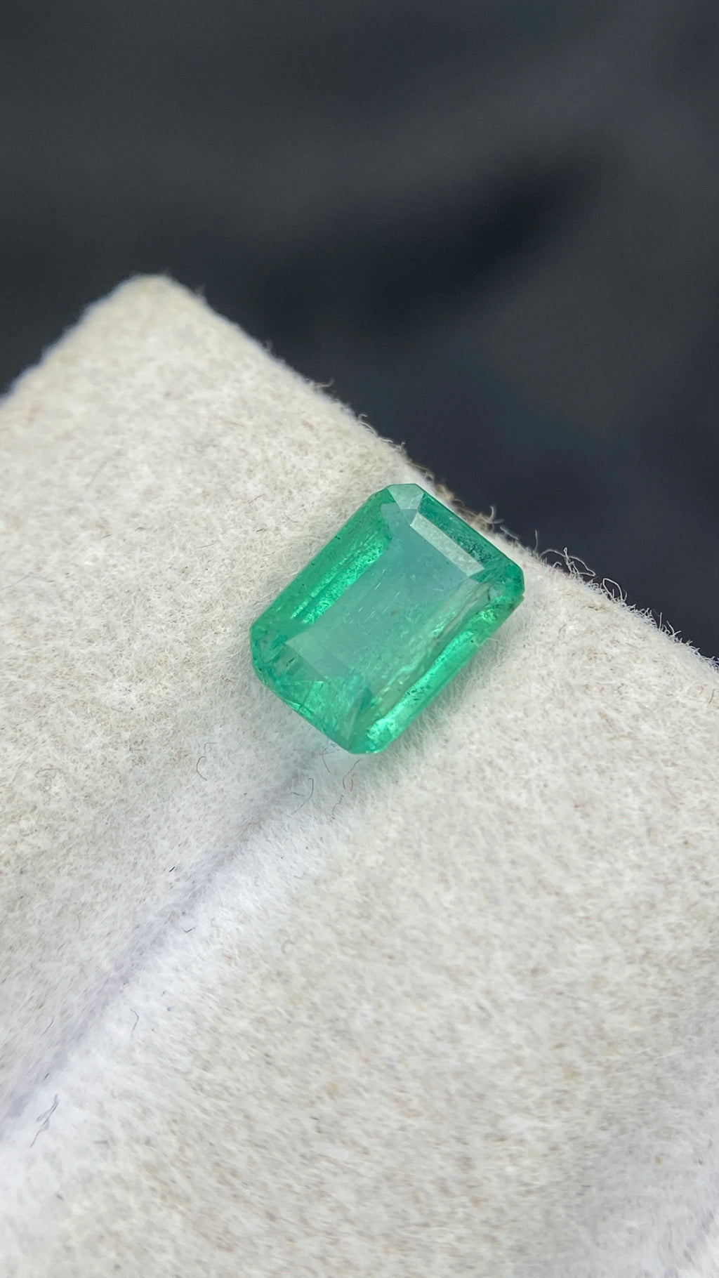 Loose emerald-cut green gemstone, angled close-up on white felt pad