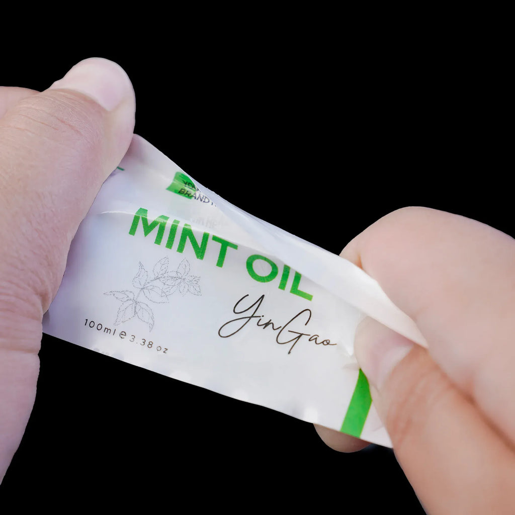 Small rectangular Mint Oil label sticker on white adhesive backing, held in hands.