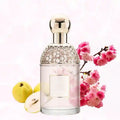 Clear perfume bottle with gold honeycomb cap, round stopper, and blank label, flanked by yellow quince and pink flowers.