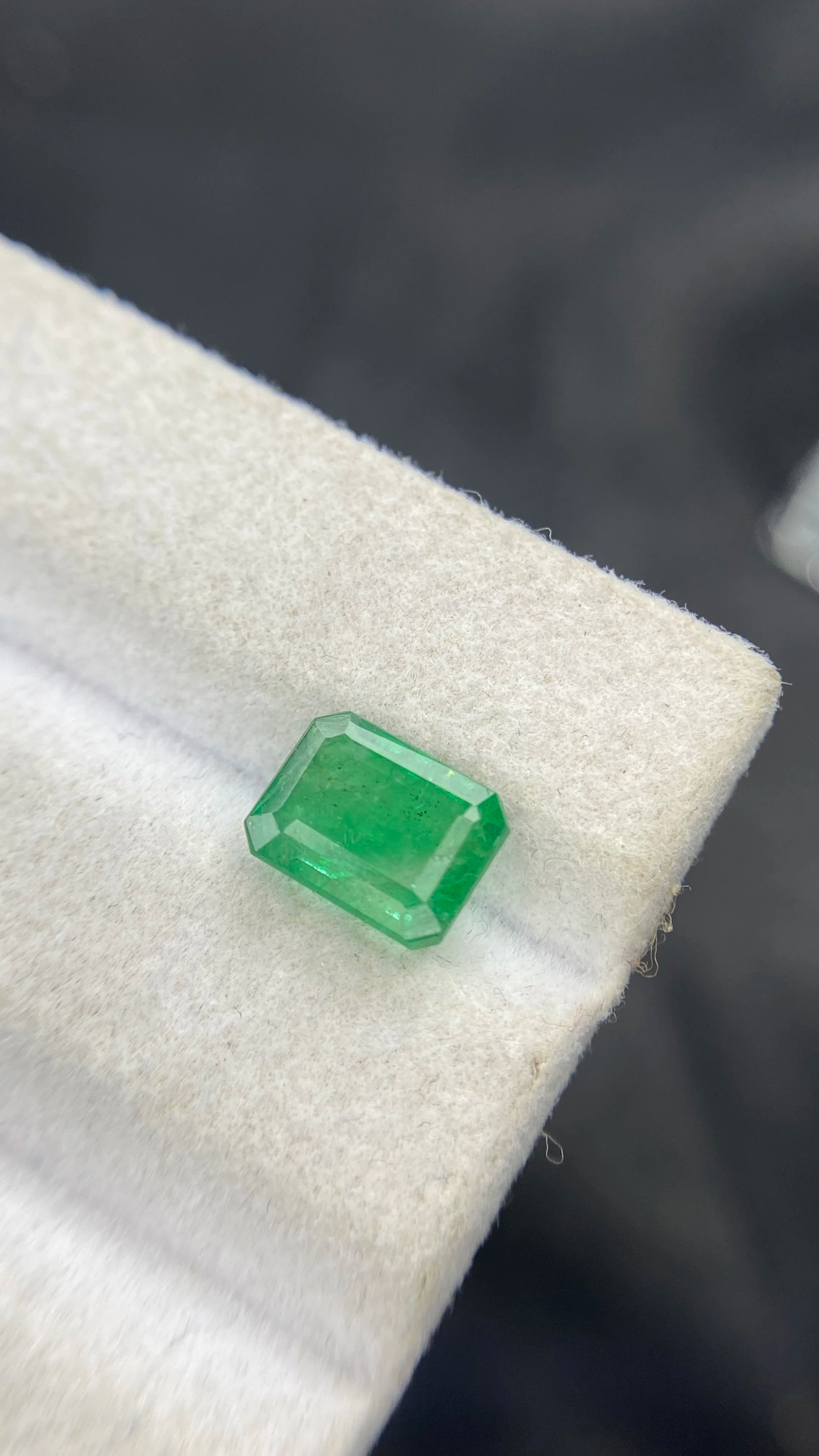 Green emerald-cut loose gemstone on white jewelry pad, angled view