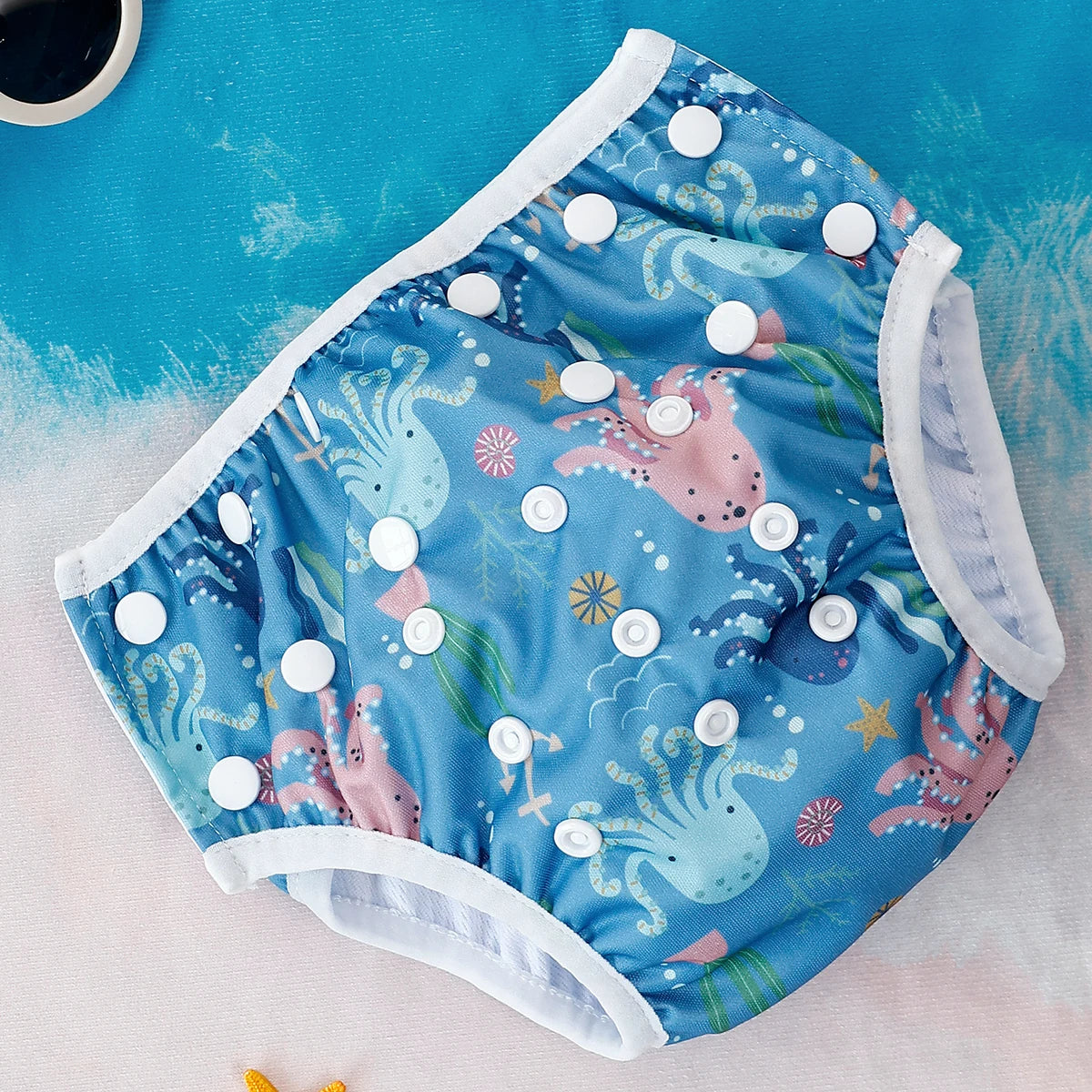 Reusable baby swim diaper in blue with octopus print and white snap buttons. Adjustable infant waterproof diaper.