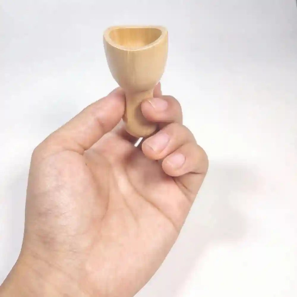 A hand holds a small, smooth, light-colored wooden facial massage cup against a plain white background.