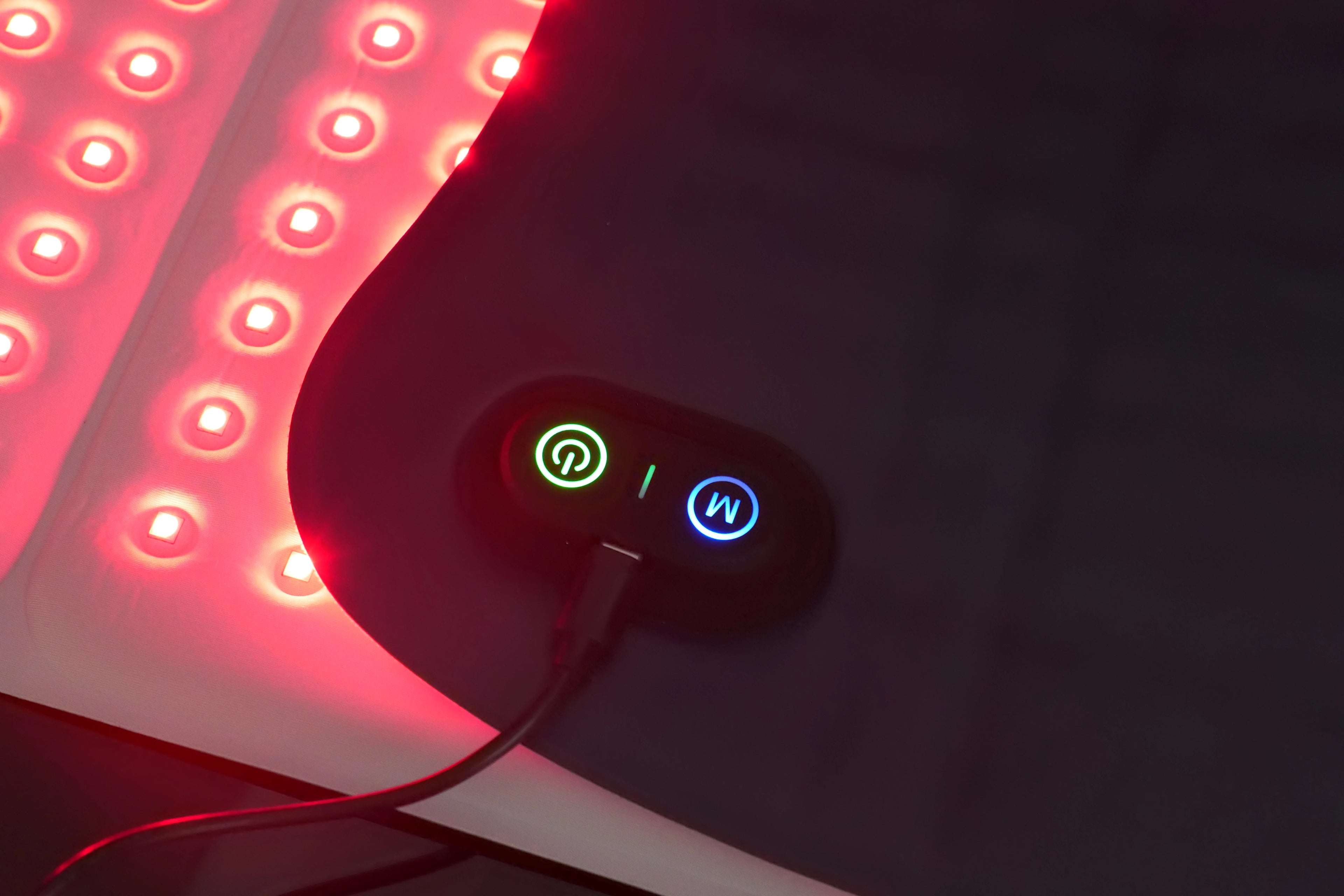 Red light therapy mat with bright LED array and a black controller featuring illuminated power and mode buttons.