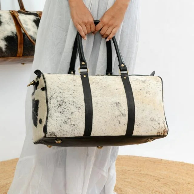 Unisex weekender duffel in white and black cow hair-on-hide leather with black trim and brass hardware.