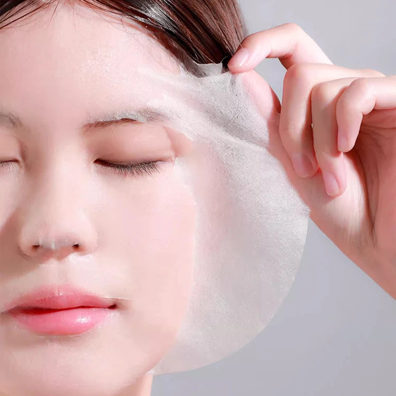 A woman applying a sheer, ultra-thin white disposable facial mask sheet to her face.