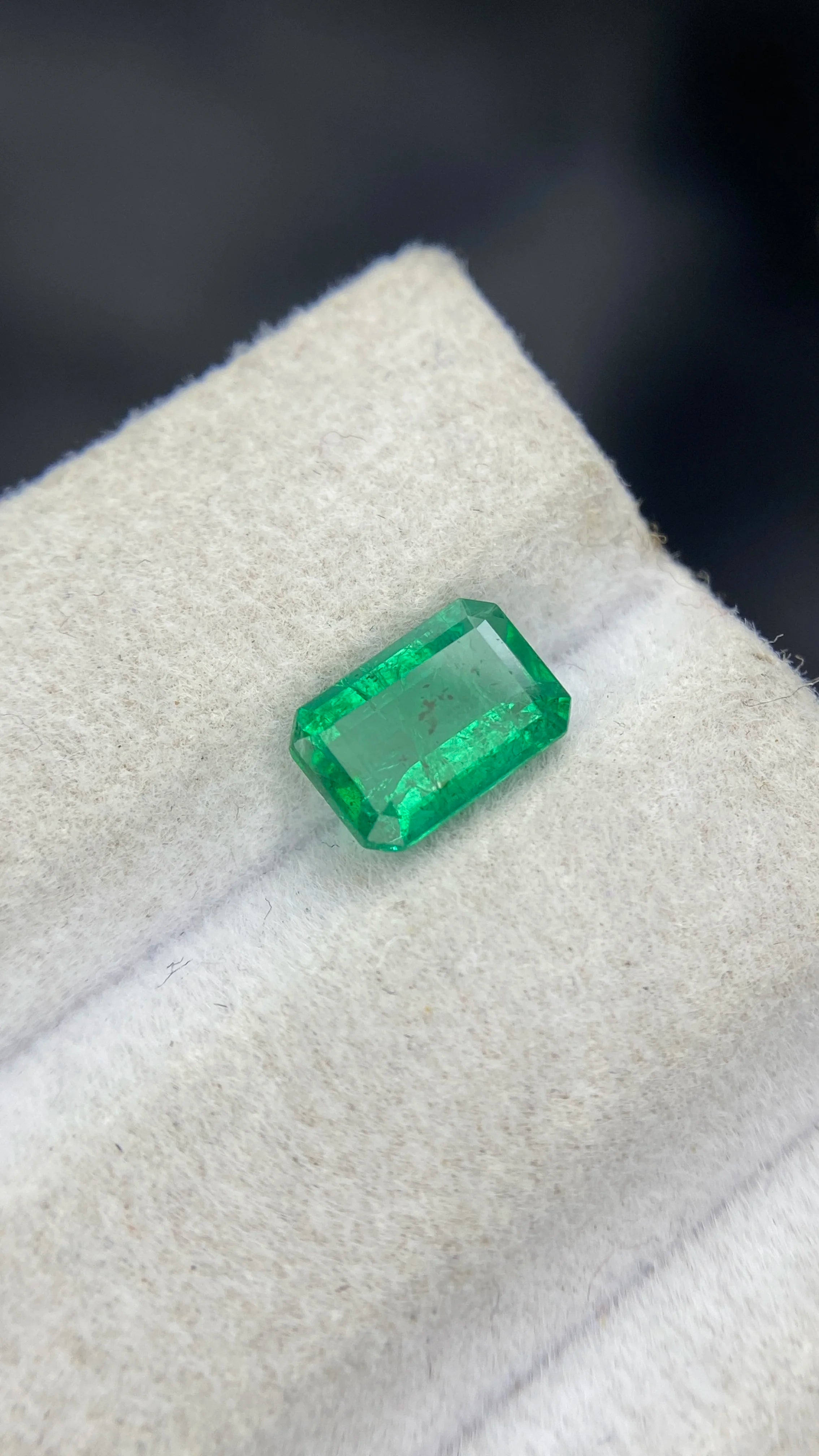 Loose green emerald-cut gemstone, angled view showing step-cut facets
