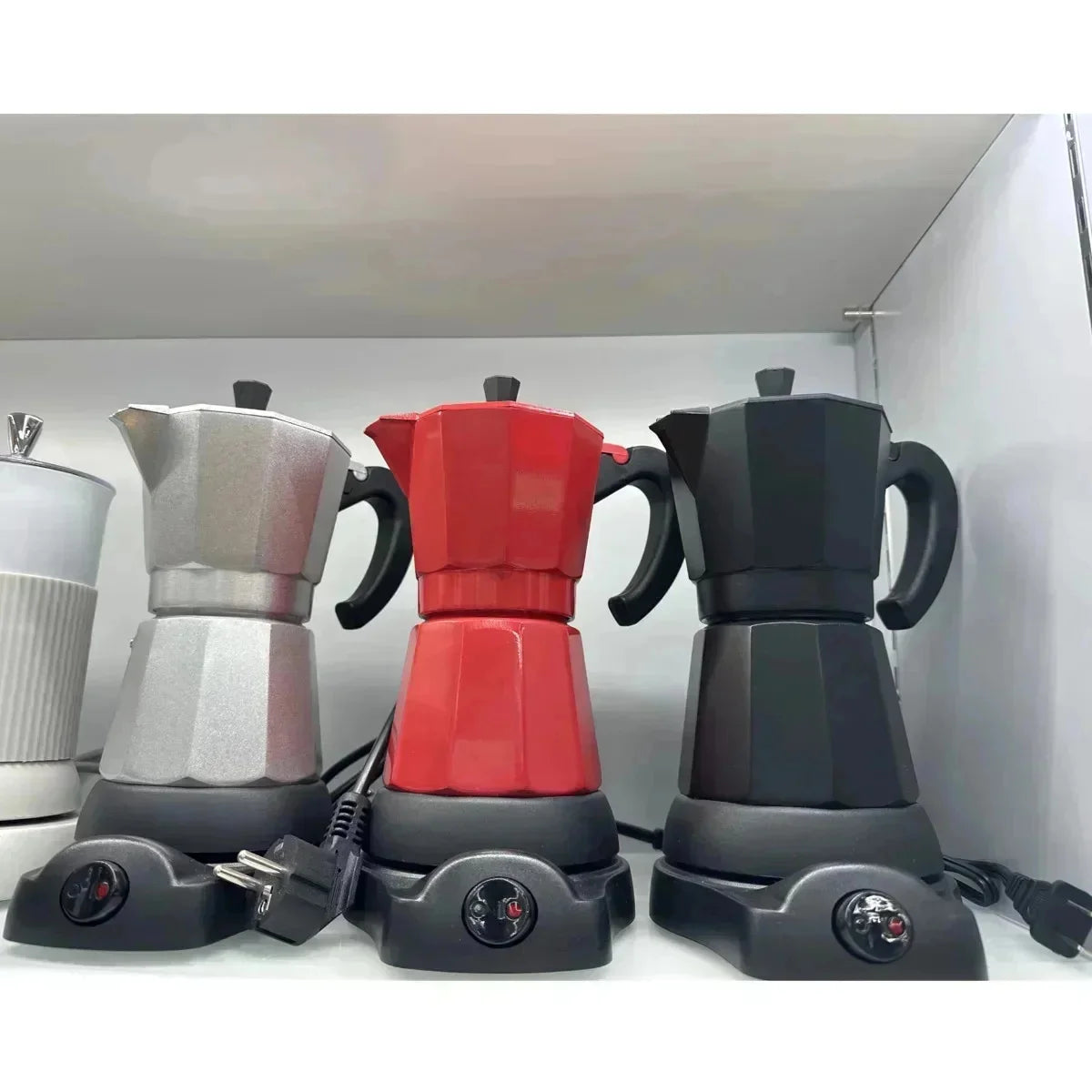 Electric Moka pot coffee makers in silver, red, and black on individual heating bases with power switches.