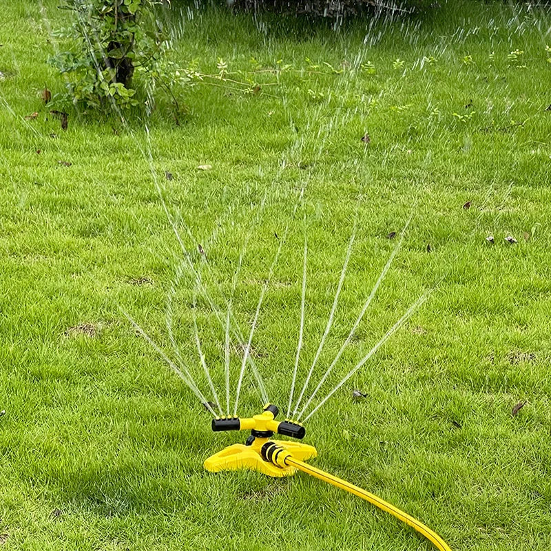 Yellow 360 rotary sprinkler spraying water from rotating nozzle arms on a lawn
