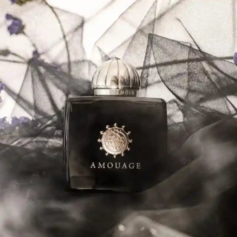 Memoir perfume in a square, black glass bottle with a silver dome cap and ornate emblem, set against black netting.
