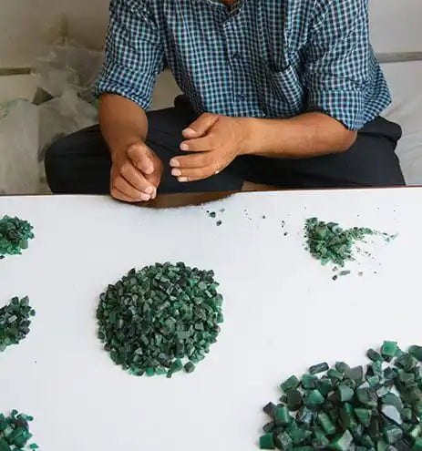 Loose green emerald chips and small cut pieces on a white surface
