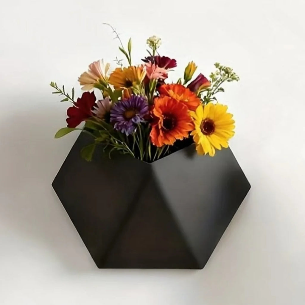 Black hexagonal wall planter with mounting holes, holding colorful flowers