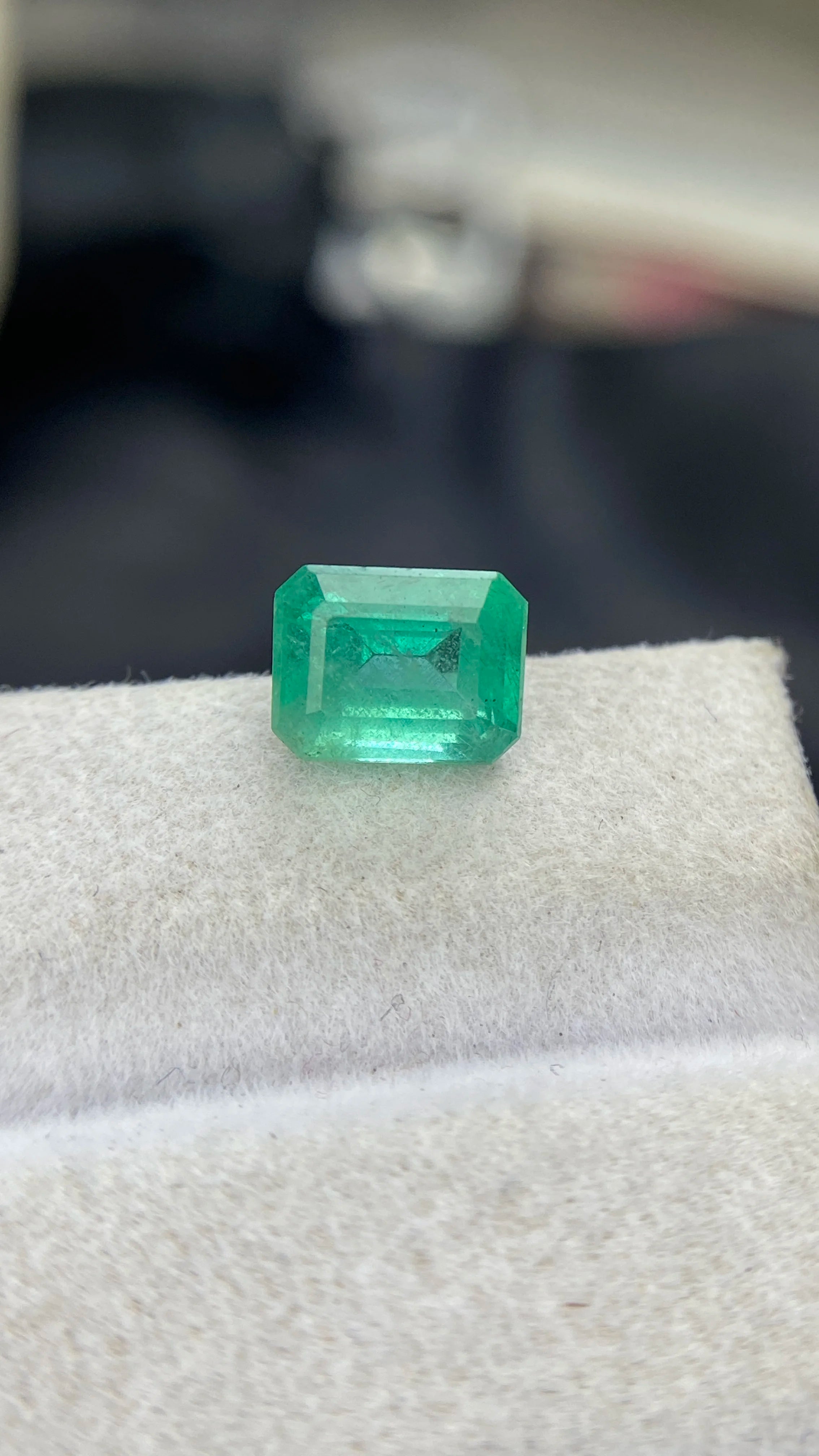 Emerald-cut green gemstone with step facets on white felt