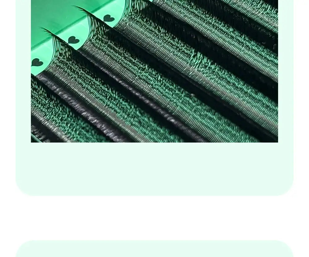 Rows of black faux mink U-shaped premade lash fans on a green tray with small heart icons.