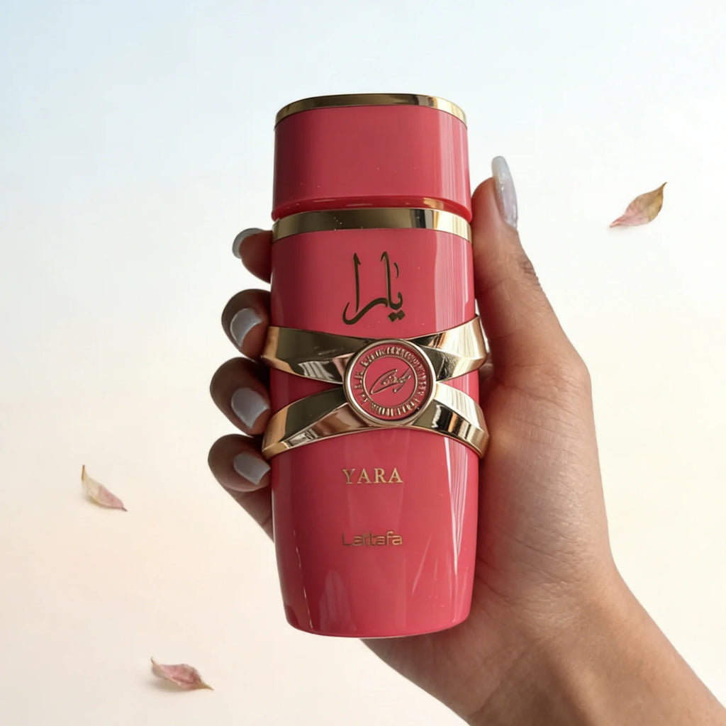 Lattafa Yara Candy perfume bottle in glossy pink with gold metallic accents held in a hand against a white background.