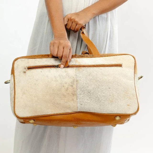 Western style brown genuine leather and hair-on-hide travel duffel trunk bag with zipper pocket and metal feet.
