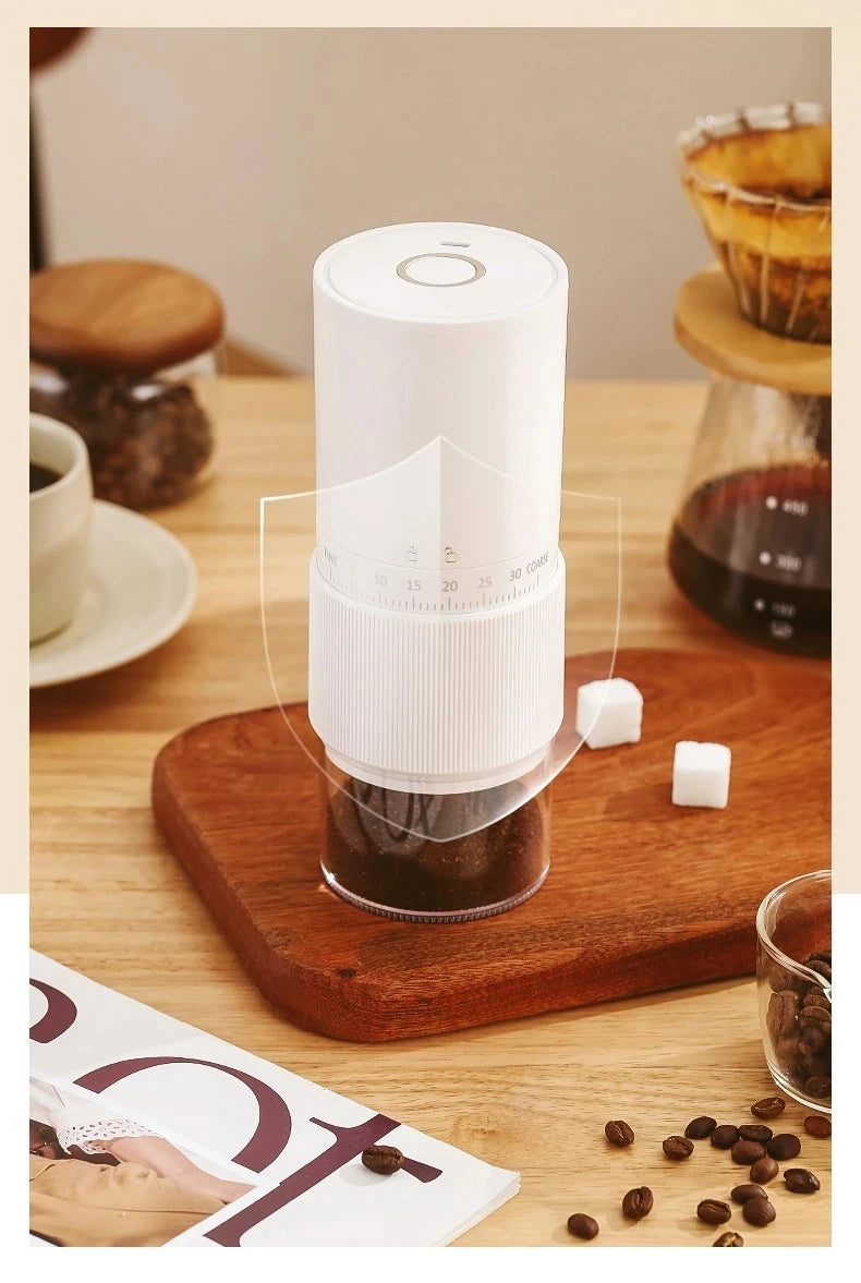 White portable electric coffee grinder with adjustable grind settings and clear grounds container on wooden table.