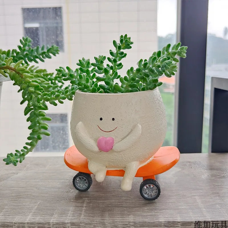 Mini succulent planter character, white pot with smile and pink heart on orange cart wheels.