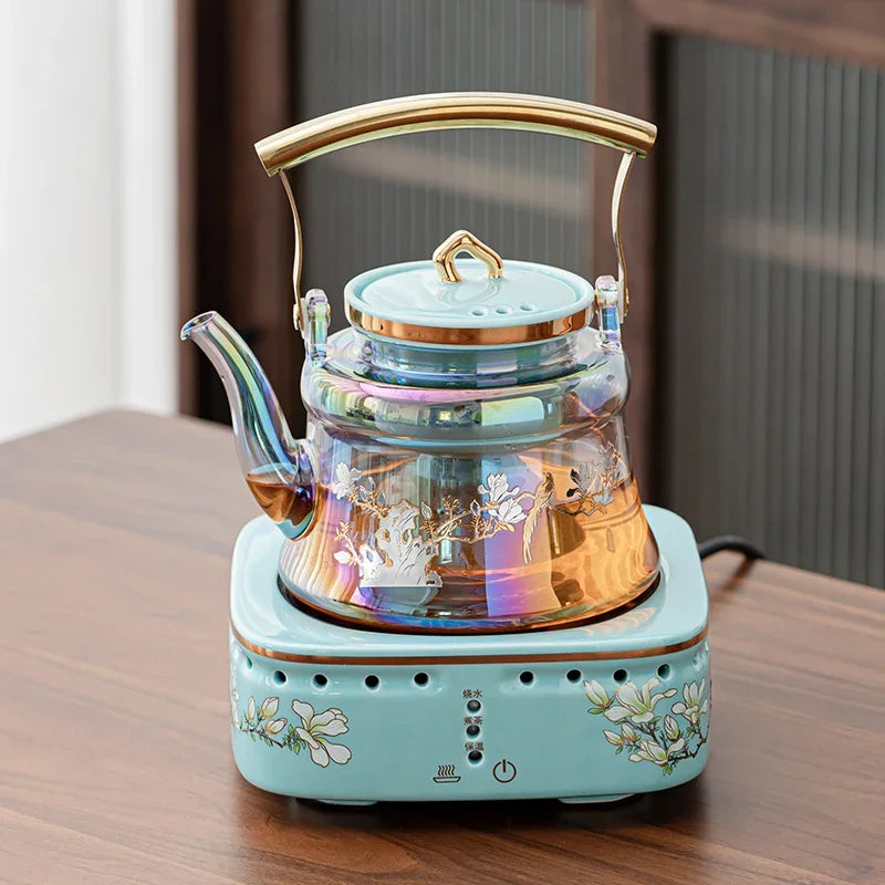 Iridescent glass electric tea kettle with floral base and gold handle on a matching ceramic floral heating stand.