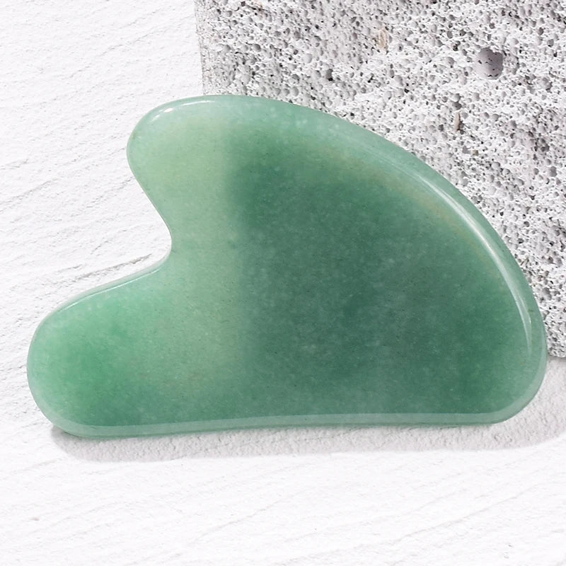Smooth, heart-shaped green jade gua sha facial massage tool resting on a textured white surface.