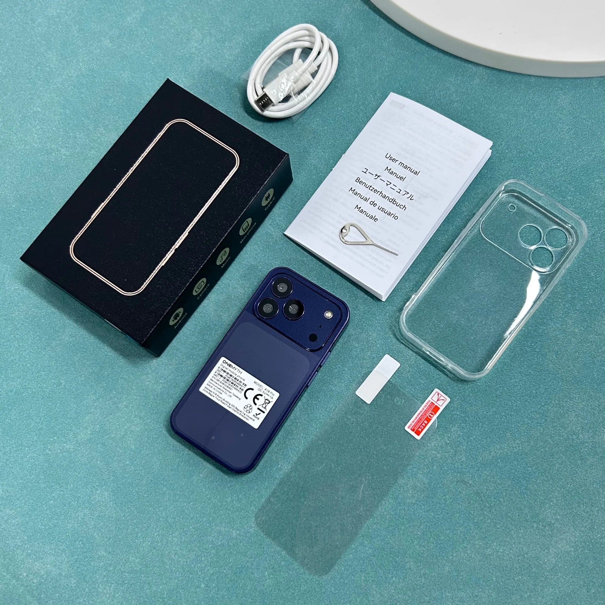 Blue ONEMYTH A18 Pro 4G mini smartphone set with box, manual, case, and charging cable on a green background.