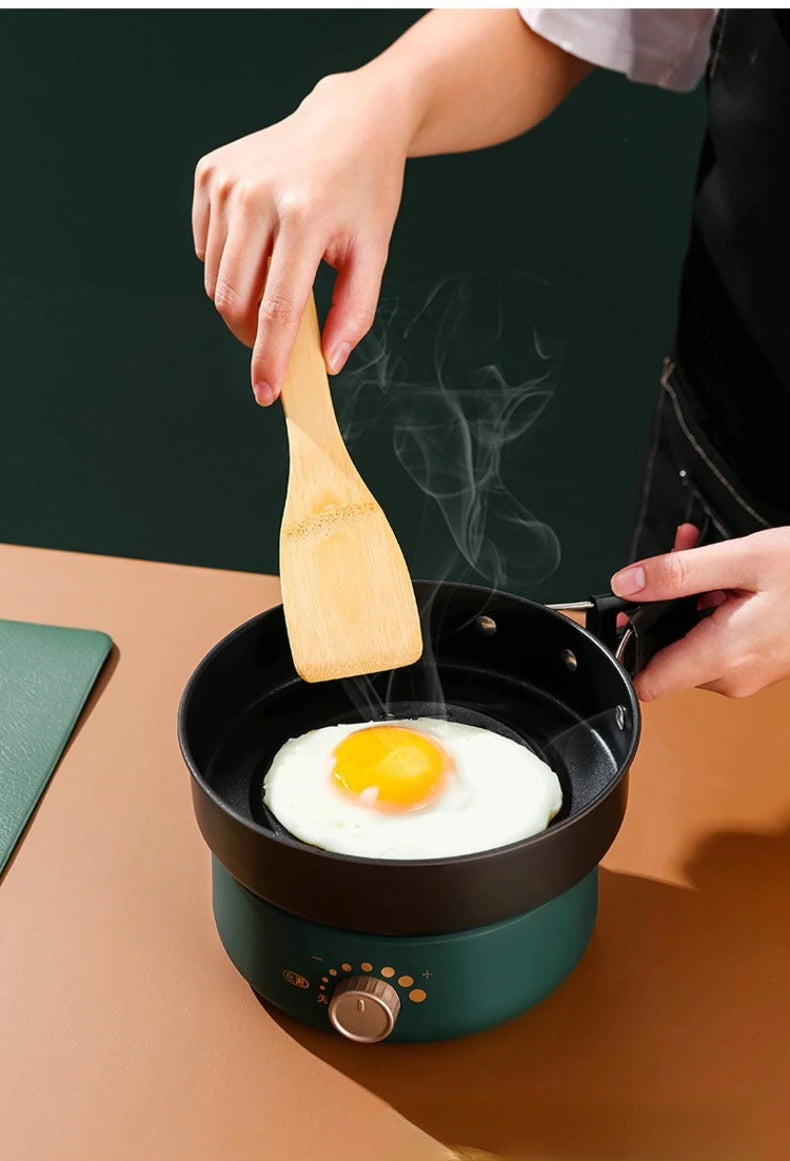 Compact electric cooker with lid, knob dial, and wooden spatula lifting egg