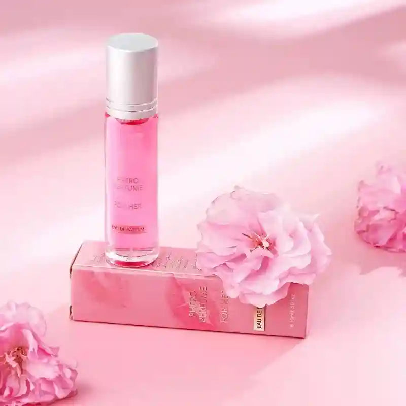 Pink roll-on pheromone perfume bottle and box on a matching pink background decorated with pink flowers.