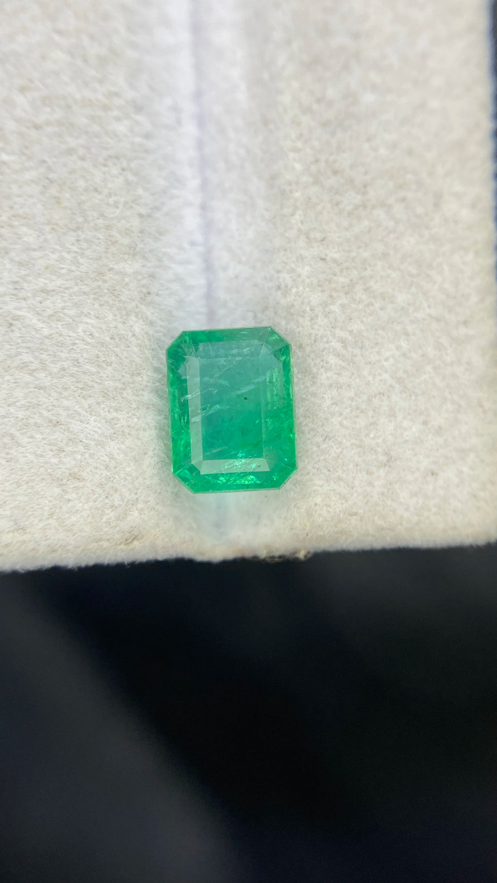 Green emerald-cut octagon loose gemstone on white cloth, top-facing step facets