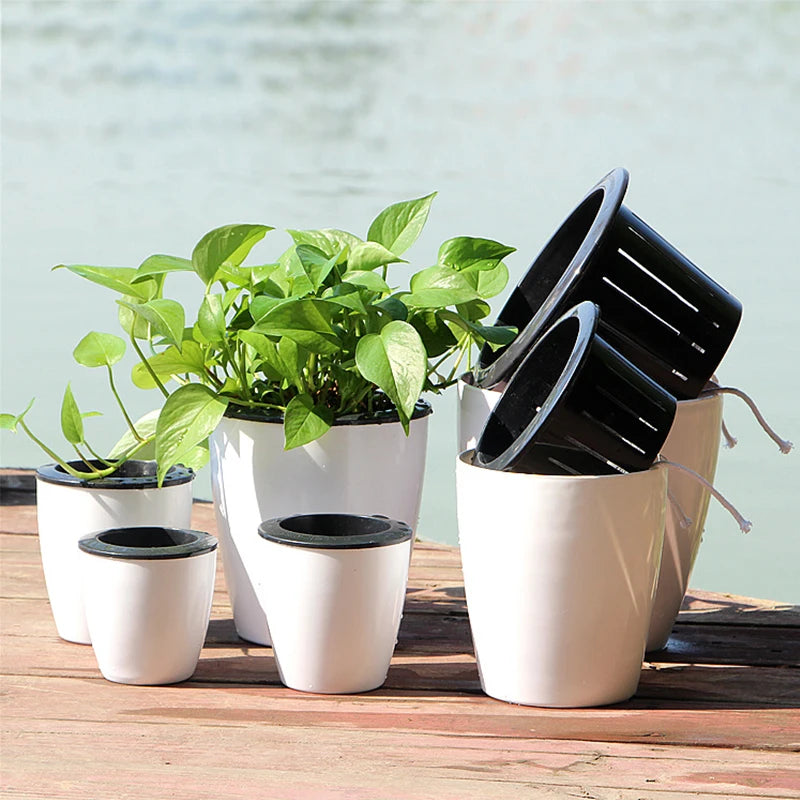 White self-watering plant pots set with black inner water bases on a wooden deck.