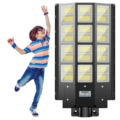 Black LED solar street light with multiple bright panels shown next to a jumping boy for scale.