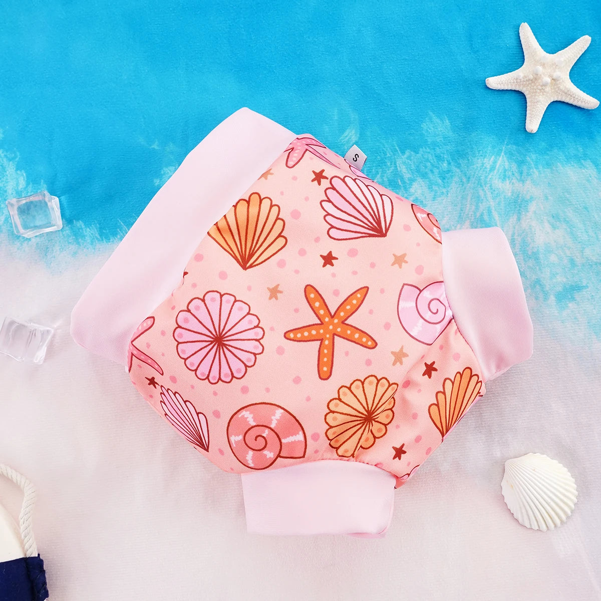Small baby swim diaper with pink seashell and starfish print on a beach background.