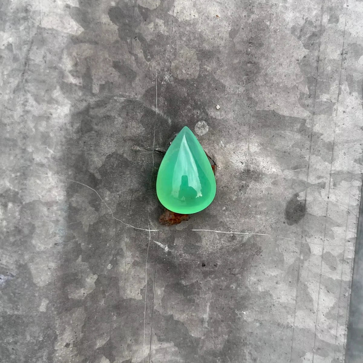 Green chrysoprase pear-shaped cabochon gemstone, polished teardrop on gray stone surface.