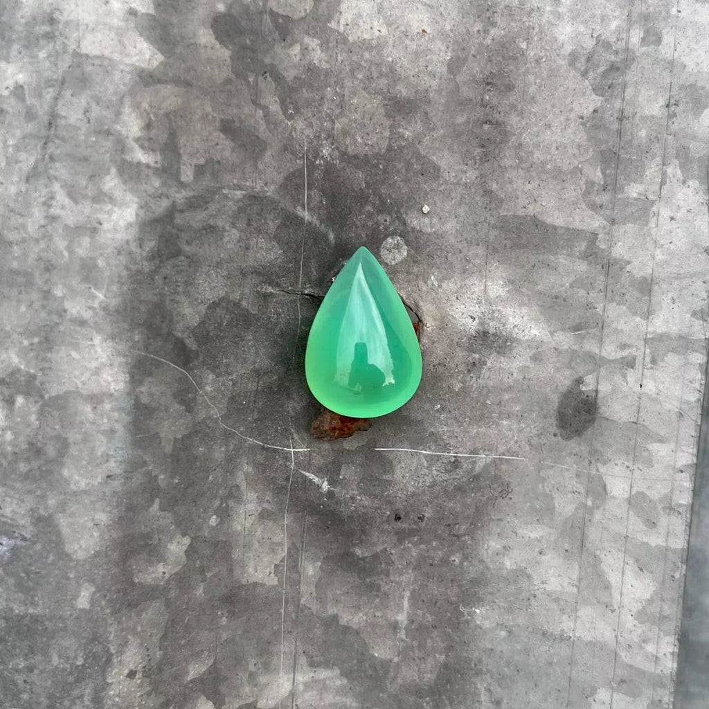 Green chrysoprase pear-shaped cabochon gemstone, polished teardrop on gray surface.