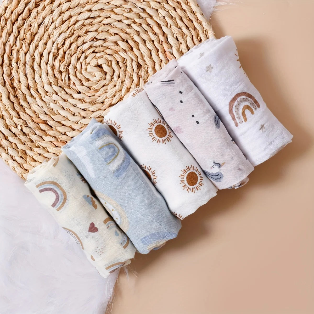 Set of 5 baby care muslin swaddle blankets with boho rainbow, sun, and star prints on a textured placemat background.