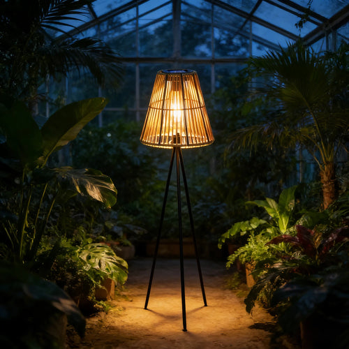 Handmade rattan solar floor lamp with a black tripod base, casting warm light among indoor plants.
