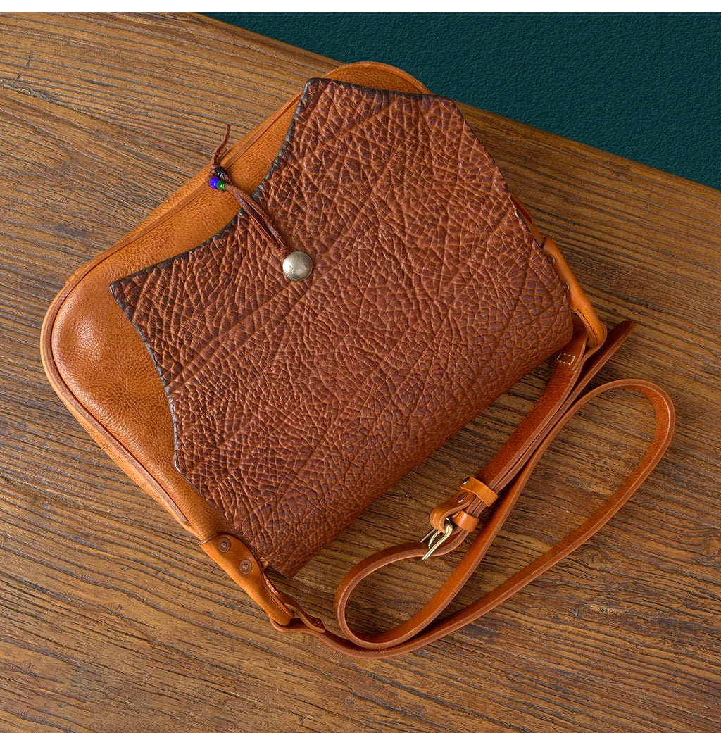 PNDME vintage handmade genuine cowhide leather messenger bag with textured flap, brass snap, and adjustable strap.