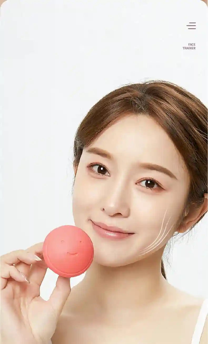A woman holding a small, round, pink silicone face-slimming exerciser with a smiley face embossed on it.