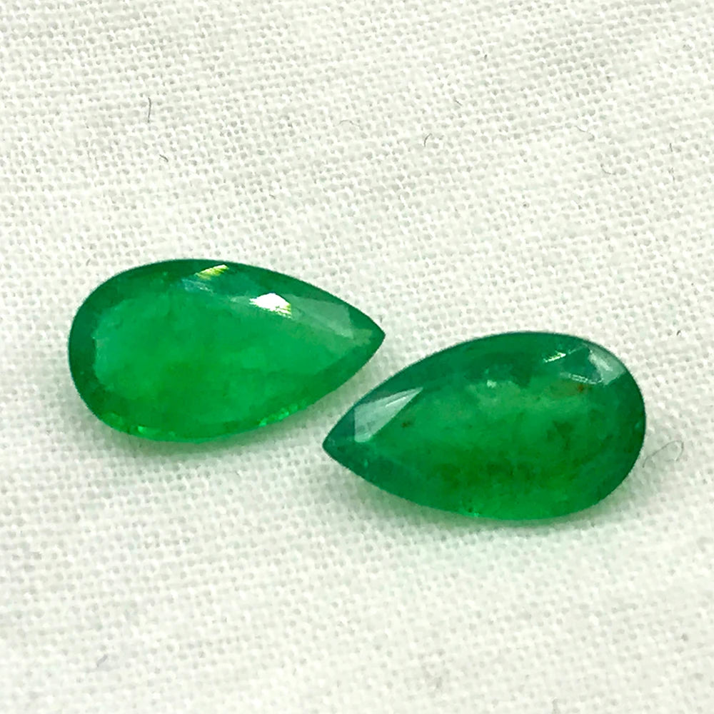 Two green teardrop gemstone cabochons on textured fabric, shiny finish