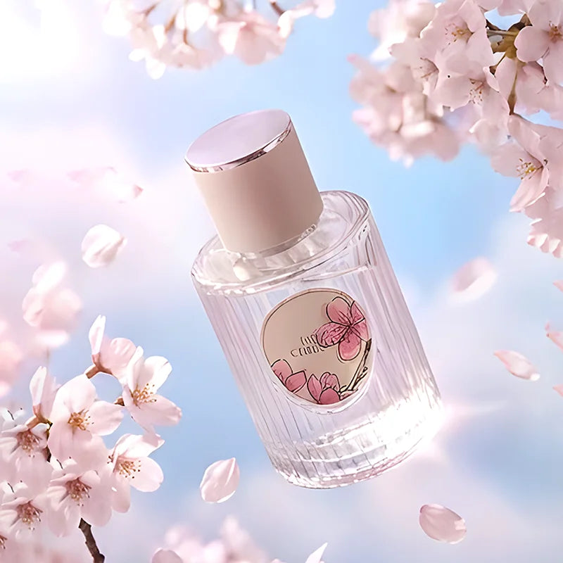 Glass perfume bottle with pink cherry blossom label, pale pink cap, surrounded by sakura flowers against blue sky.