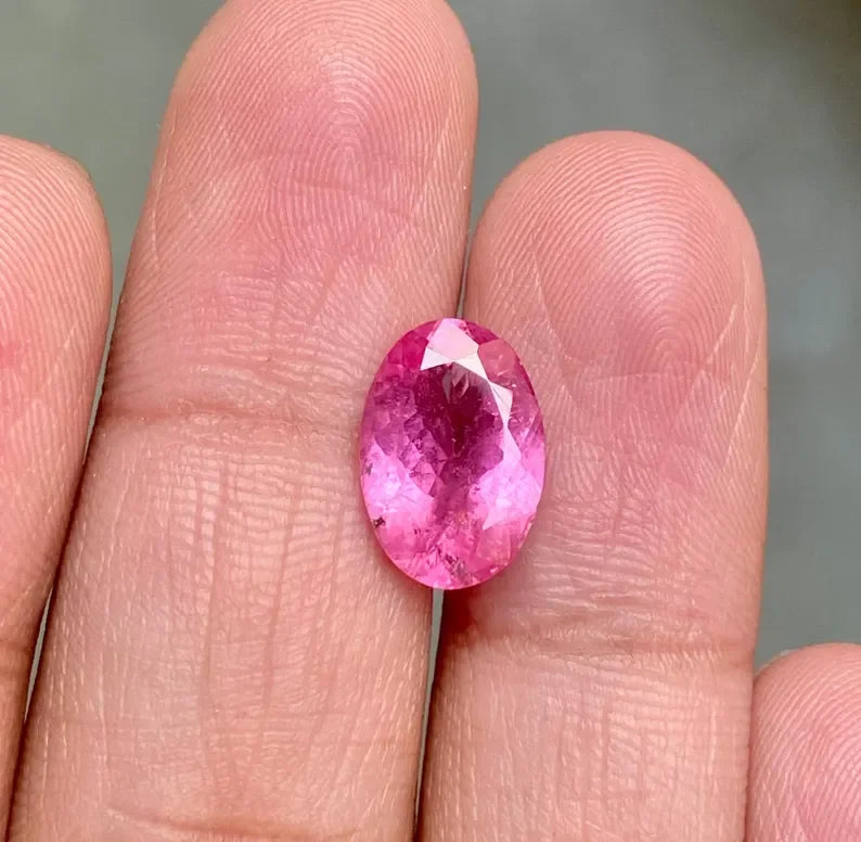 Oval-cut pink sapphire gemstone with faceted top, held between fingers