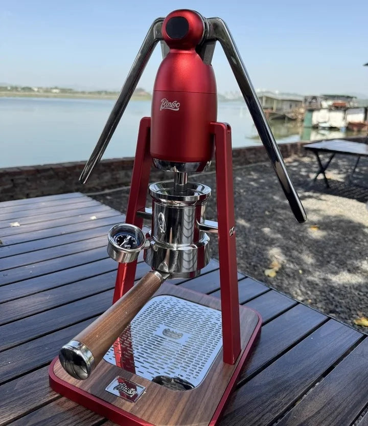 Binco red manual lever espresso maker with chrome components, pressure gauge, and wood handle on a wooden base.