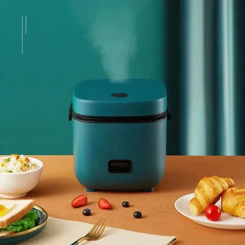 Mini electric rice cooker with teal body and black lid rim, side handle visible.