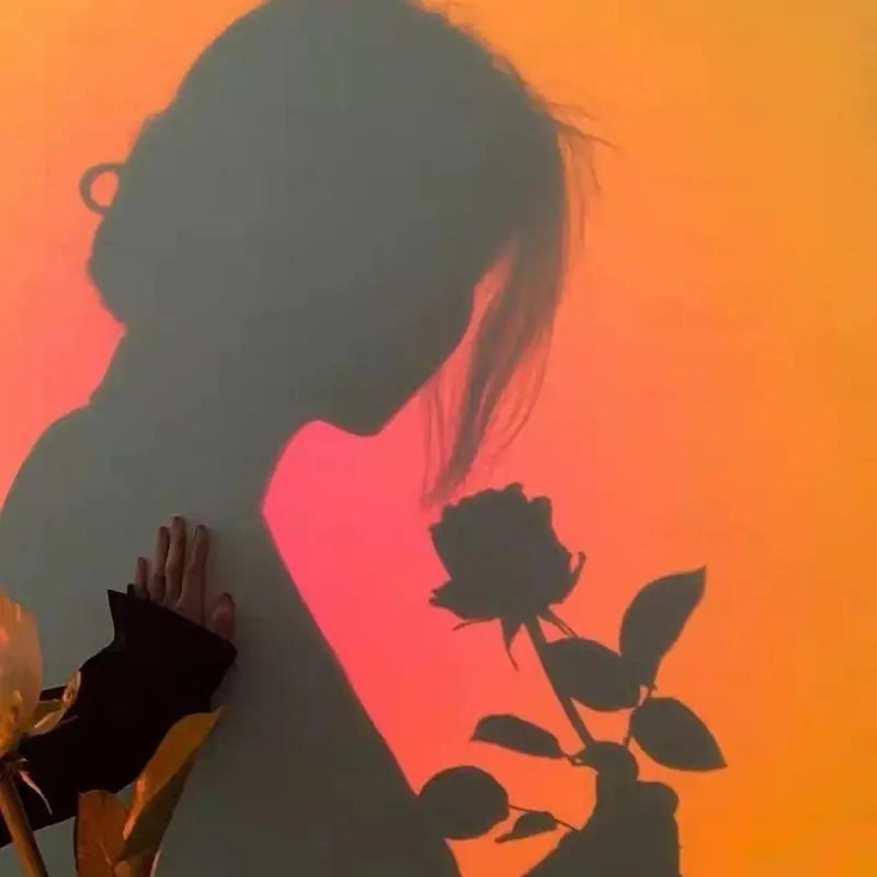 Sunset lamp casting a warm, gradient orange-to-pink glow against a wall to create artistic silhouettes of a person.