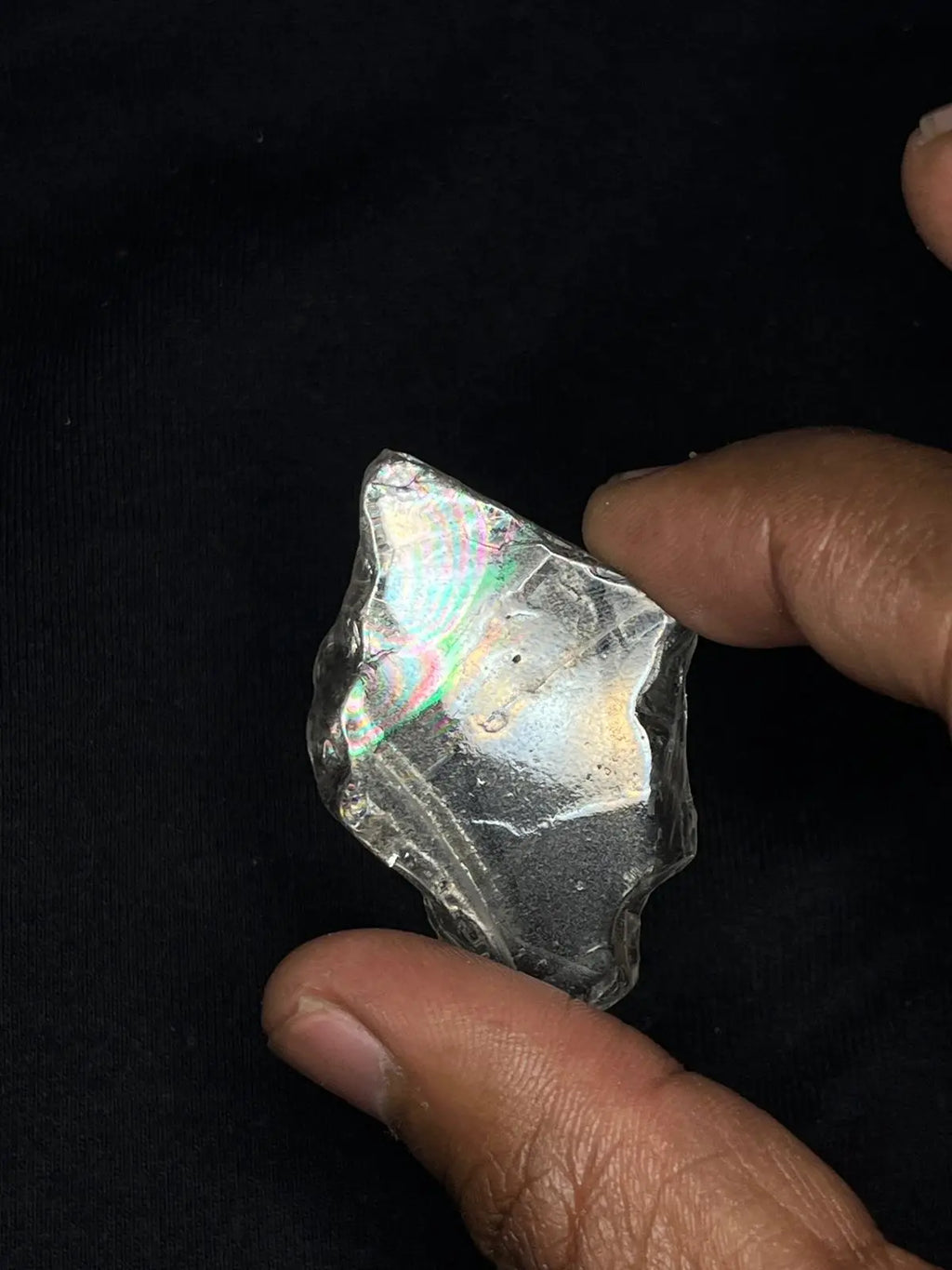 Hand holding dark iridescent rough gemstone, reflective rainbow surface