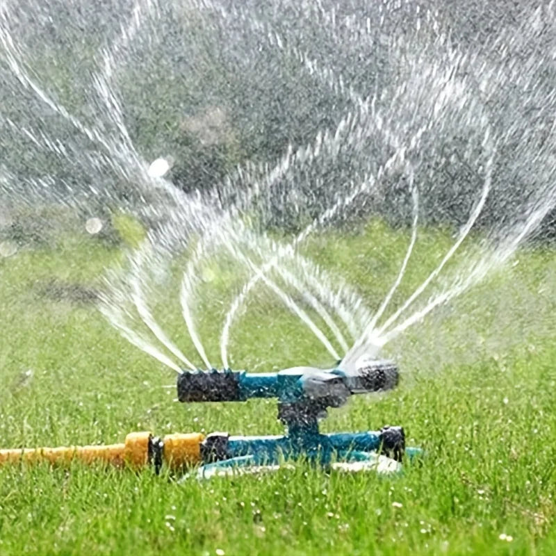 Rotary sprinkler with rotating arms spraying a wide fan pattern over grass.