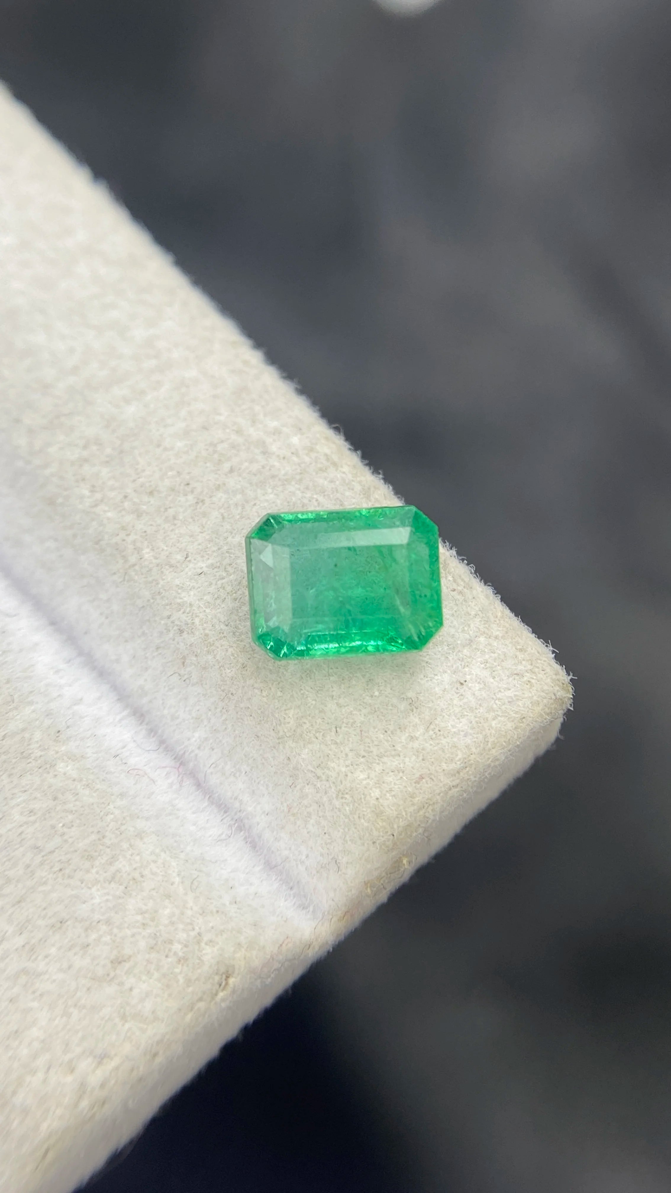 Loose green emerald-cut gemstone at slight angle, step facets visible