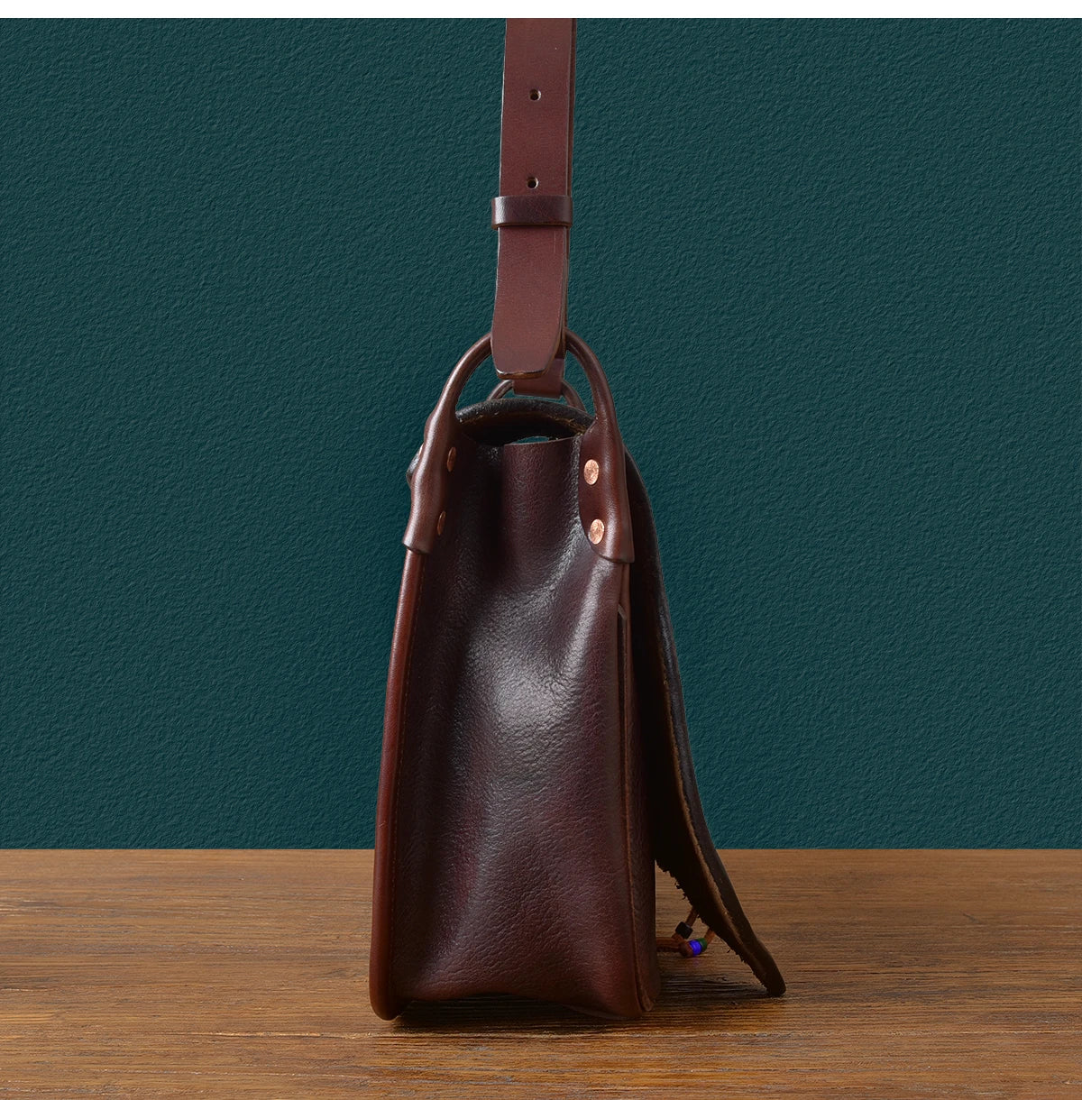 Side view of a handmade brown genuine cowhide messenger bag, vintage designer style with adjustable leather strap.